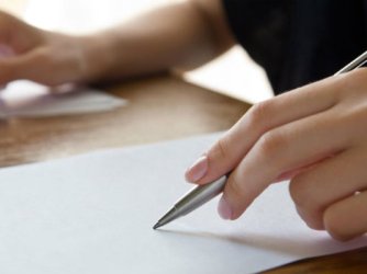 A hand holding a pencil on a piece of plain paper.