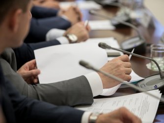 politician sitting by table with his hands over document during political summit or conference