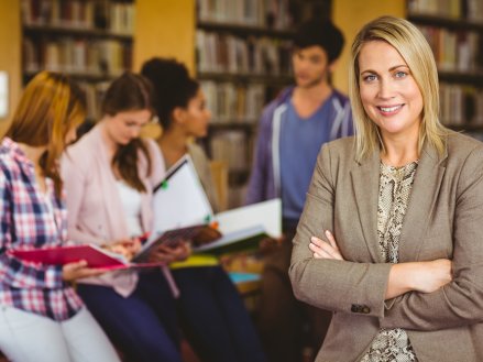 Professor looking at camera with arms folded in library