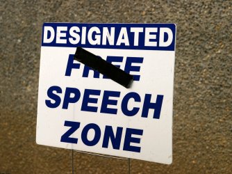 Sign reading "Designated Free Speech Zone" with "Free" crossed out.