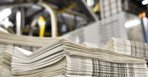 stack of freshly printed daily newspapers transported to a printing plant, in the background machines and technical equipment of a large printing plant