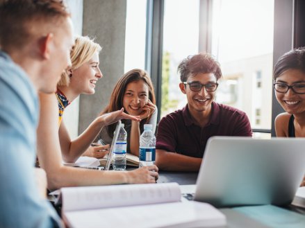 College students gathered around a table looking at a computer.