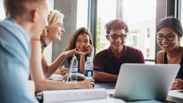 College students gathered around a table looking at a computer.