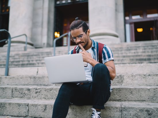 College student on steps looking at laptop